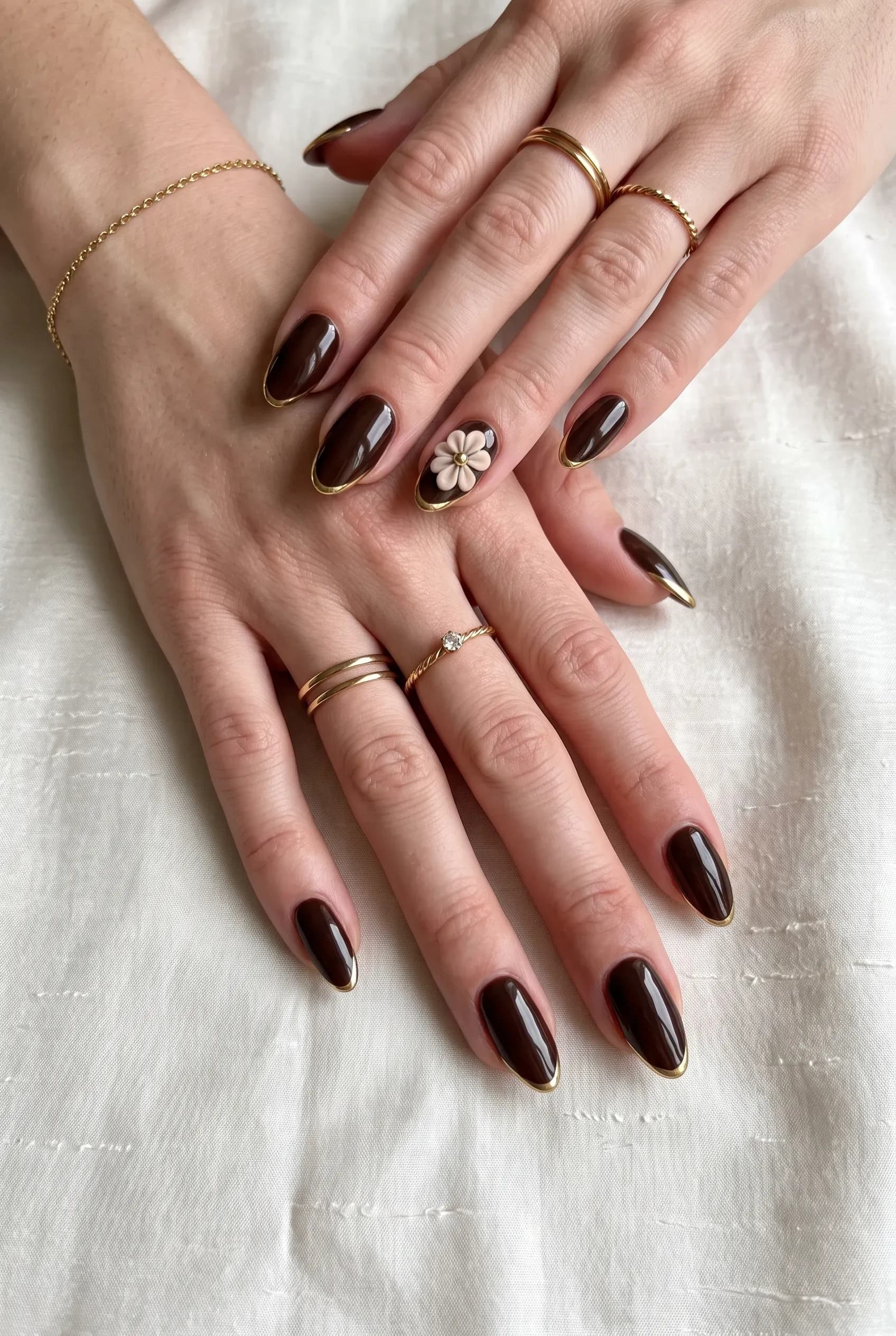 Glossy dark chocolate almond nails with gold outline tips and a 3D beige flower